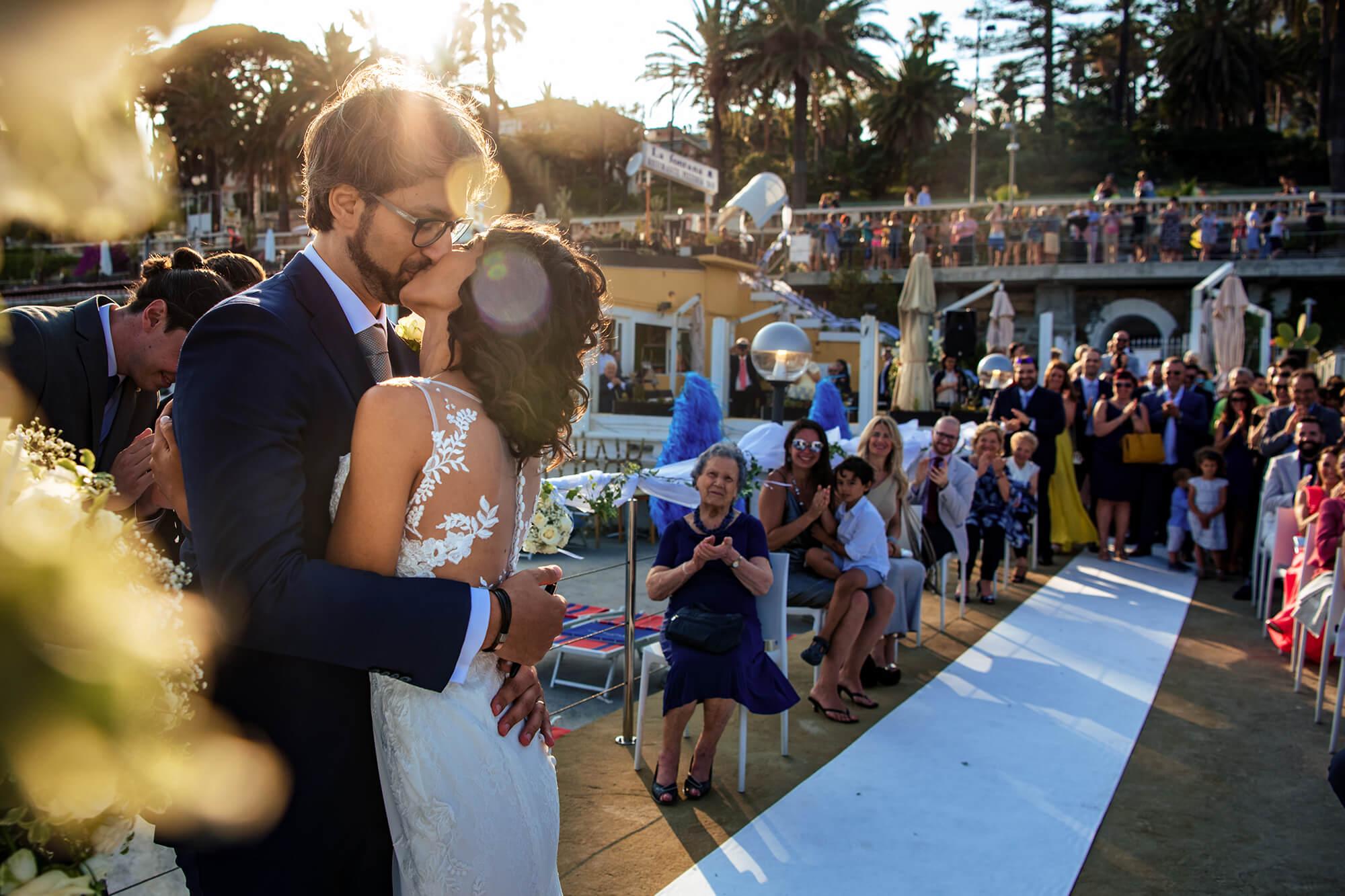 una foto di un matrimonio in spiaggia a Sanremo, gli sposi si baciano all'altare davanti a tutti gli ospiti.